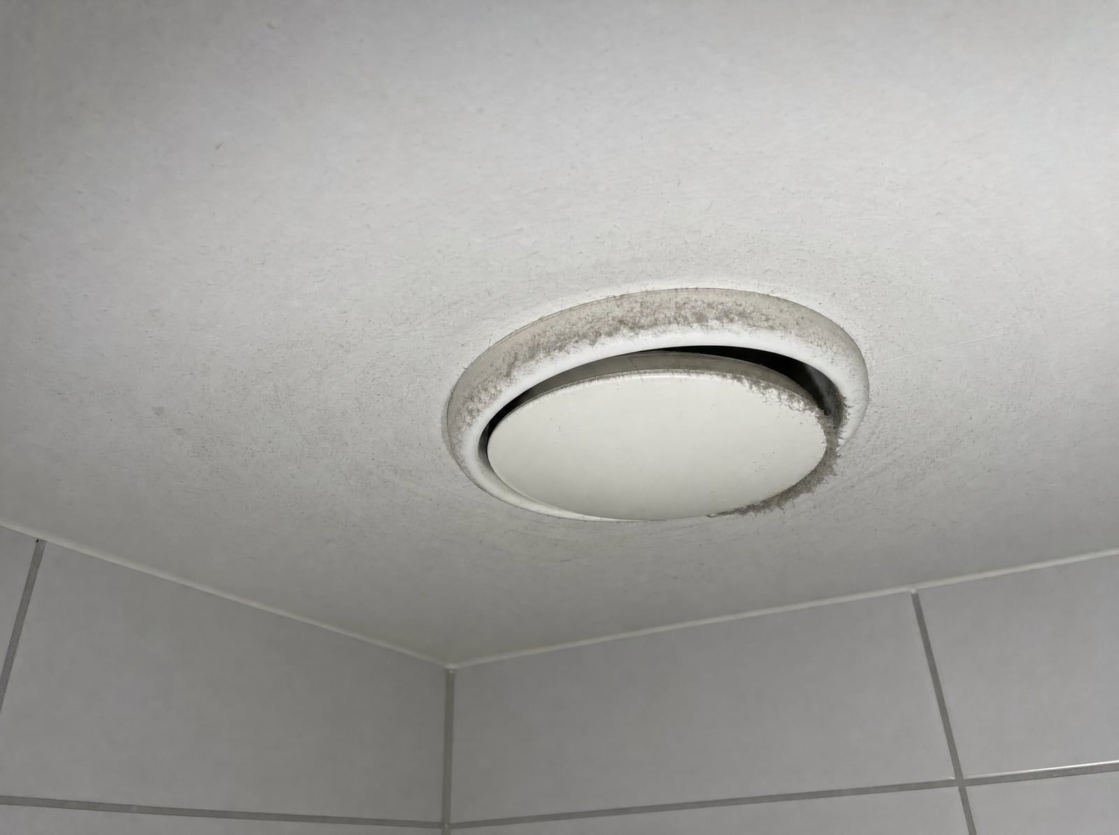 Avtrekksventil i baderomstaket med grått støv rundt kanten